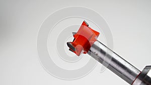 Forstner bit with a red metal cutter rotating in an electric drill on a white background.