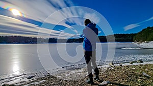 Forstsee - Rear view of man with hiking backpack watching the frozen lake Forstsee, Techelsberg, Carinthia (Kaernten), Austria,