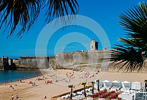 Fort in Torre beach, blue sky and ocean waves, yellow brown sand, people walking in the sand