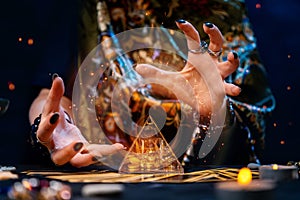 A fortune teller conjures a glass pyramid. Magical aura and sparks around the pyramid. Close-up. The concept of divination, magic photo