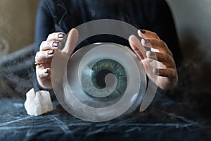 Fortune teller holds hands above magic crystal ball with eyeball inside. Conceptual image of black magic and occultism