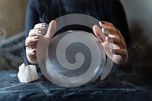 Fortune teller holds hands above magic crystal ball with smoke around. Conceptual image of black magic and occultism