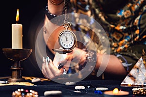 A fortune teller holds a watch on a chain in her hands, guessing for the future. Glowing magical aura around the clock. The