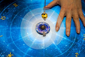 Fortune teller with magic pendulum on blue horoscope like astrology, zodiac. esoteric topic