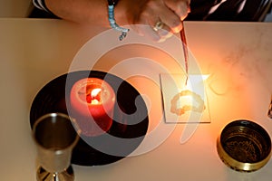 Portrait of beautiful middle age woman sits near a fortune teller desk with a tarot cards, black pendulum and candles.