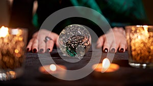 Fortuneteller divining on magic ball at table with burning candles