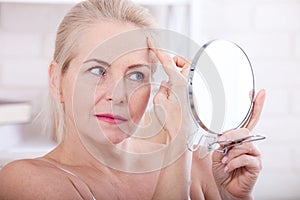 Forty years old woman looking at wrinkles in mirror. Plastic surgery and collagen injections. Makeup. Macro face. Selective focus