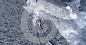 Forward aerial top view over hairpin bend turn road in mountain snow covered winter forest.White pine tree woods.Snowy