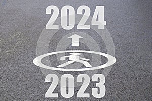 Forward arrow sign for a pedestrian on the asphalt, 2024 ahead and 2023 below, traffic in the New Year 2024, going into