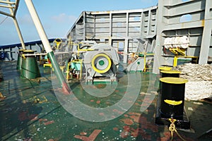 Forward mooring station behind windbreaker with winch and anchor windlass with chain and heaved up white manila rope.