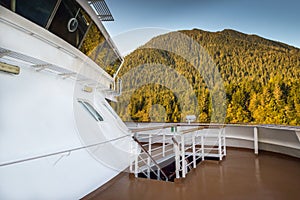 Forward outside upper deck below cruise ship bridge passing by Alaska Inside Passage natural scenery.