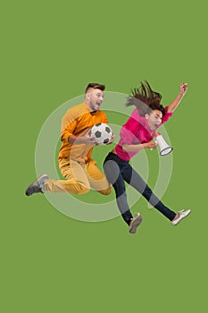 Forward to the victory.The young couple as soccer football player jumping and kicking the ball at studio on a green