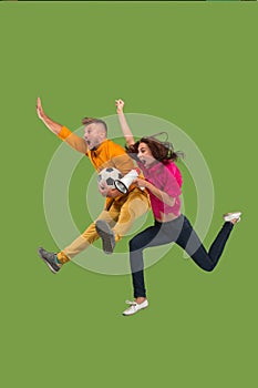 Forward to the victory.The young couple as soccer football player jumping and kicking the ball at studio on a green