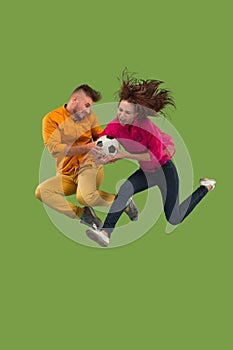 Forward to the victory.The young couple as soccer football player jumping and kicking the ball at studio on a green