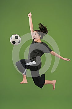 Forward to the victory.The young woman as soccer football player jumping and kicking the ball at studio on green