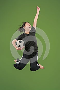 Forward to the victory.The young woman as soccer football player jumping and kicking the ball at studio on green