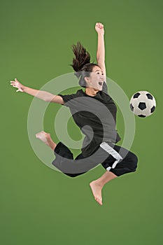 Forward to the victory.The young woman as soccer football player jumping and kicking the ball at studio on green