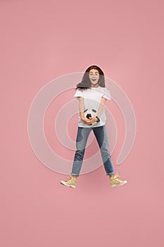 Forward to the victory.The young woman as soccer football player jumping and kicking the ball at studio on pink