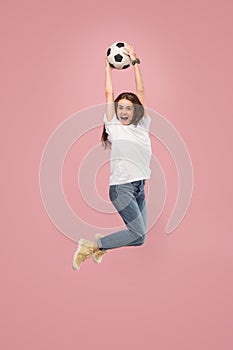 Forward to the victory.The young woman as soccer football player jumping and kicking the ball at studio on pink