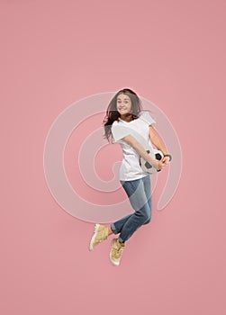 Forward to the victory.The young woman as soccer football player jumping and kicking the ball at studio on pink