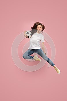 Forward to the victory.The young woman as soccer football player jumping and kicking the ball at studio on pink