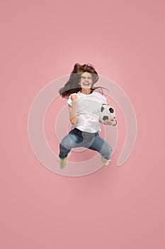 Forward to the victory.The young woman as soccer football player jumping and kicking the ball at studio on pink