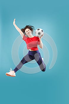 Forward to the victory.The young woman as soccer football player jumping and kicking the ball at studio on pink