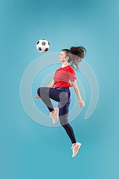 Forward to the victory.The young woman as soccer football player jumping and kicking the ball at studio on pink