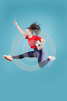 Forward to the victory.The young woman as soccer football player jumping and kicking the ball at studio on pink
