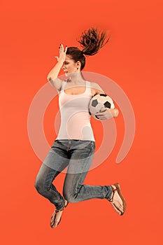 Forward to the victory.The young woman as soccer football player jumping and kicking the ball at studio on a red