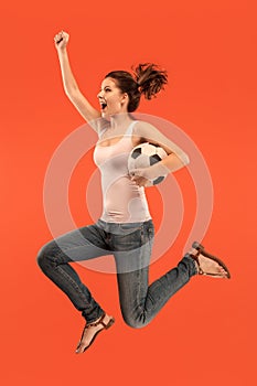 Forward to the victory.The young woman as soccer football player jumping and kicking the ball at studio on a red