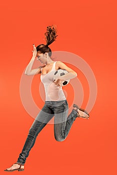 Forward to the victory.The young woman as soccer football player jumping and kicking the ball at studio on a red