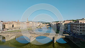 Forwards fly above Arno river in city. Old arch bridges spanning water, rows of buildings on waterfronts. Florence