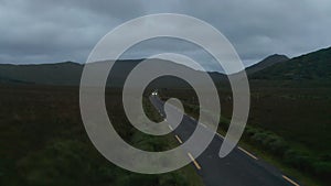 Forwards fly above narrow country and passing against car. Cloudy day at dusk. Mountain ridge in background. Ireland