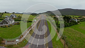 Forwards fly above road and cycling paths passing around detached houses in countryside. Aerial landscape shot. Ireland