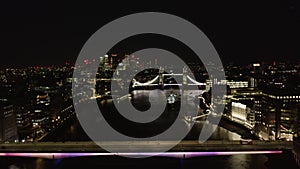 Forwards fly above Thames river at night. Heading to old touristic landmark, illuminated Tower Bridge. London, UK