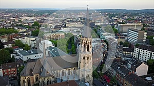 Forwards fly above town around church tower. Panoramic view of urban borough. Heilig Kreuz Kirche in Aachen, Germany