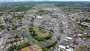 Forwards fly high above town. Sport centre and historic town borough on river bank. Aerial panoramic shot. Ennis