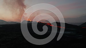 Forwards fly over volcanic landscape at dawn. Rising smoke from active volcano and flowing lava streams on ground