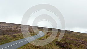 Forwards tracking convertible car on wet curvy road surrounded by meadows and grasslands in countryside. Ireland