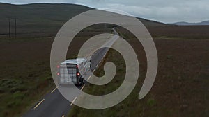 Forwards tracking of offroad car with horse trailer driving on narrow road in countryside. Pastures and grasslands along