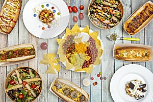 Top view photo of Mexican dishes, hot dogs, salads in home service bowl and poles with lacasitos on wooden background photo