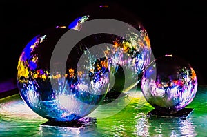 A fountain in the form of three silver steel balls. Night city lights reflected in the flowing water. Blurred motion