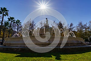 fountain with jets of water in a park of the city of Seville, rays of sun in blue sky without clouds