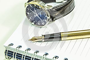 Fountain pen on blank notepad and watch