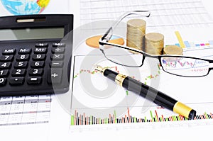 Fountain pen and eyeglasses and coins stack and calculator on stock chart report