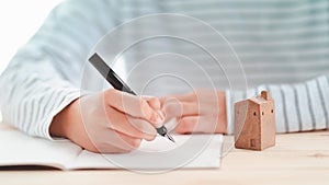 Fountain pen holding by man with small ceramic home model on desk