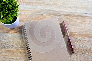 Fountain pen or ink pen with notebook paper and little decoration tree in white vase on wooden working table with copy space, off