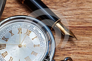 Fountain pen and pocket watch on a wooden table