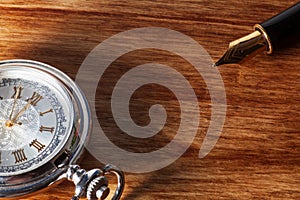 Fountain pen and pocket watch on a wooden table